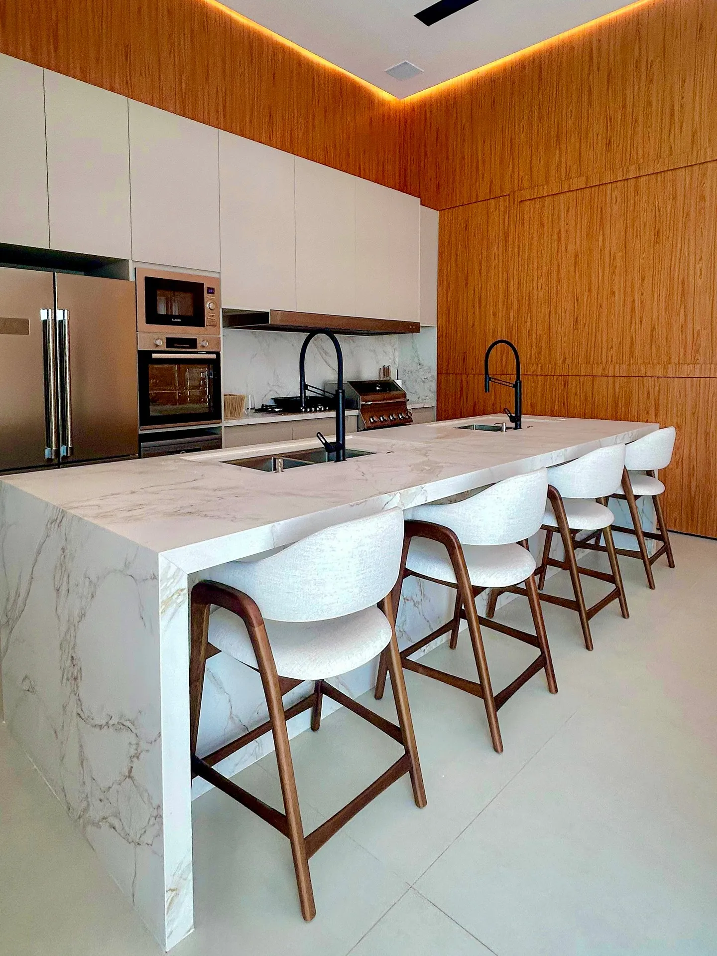 Isla de cocina en mármol Calacatta con banquetas y frente de roble